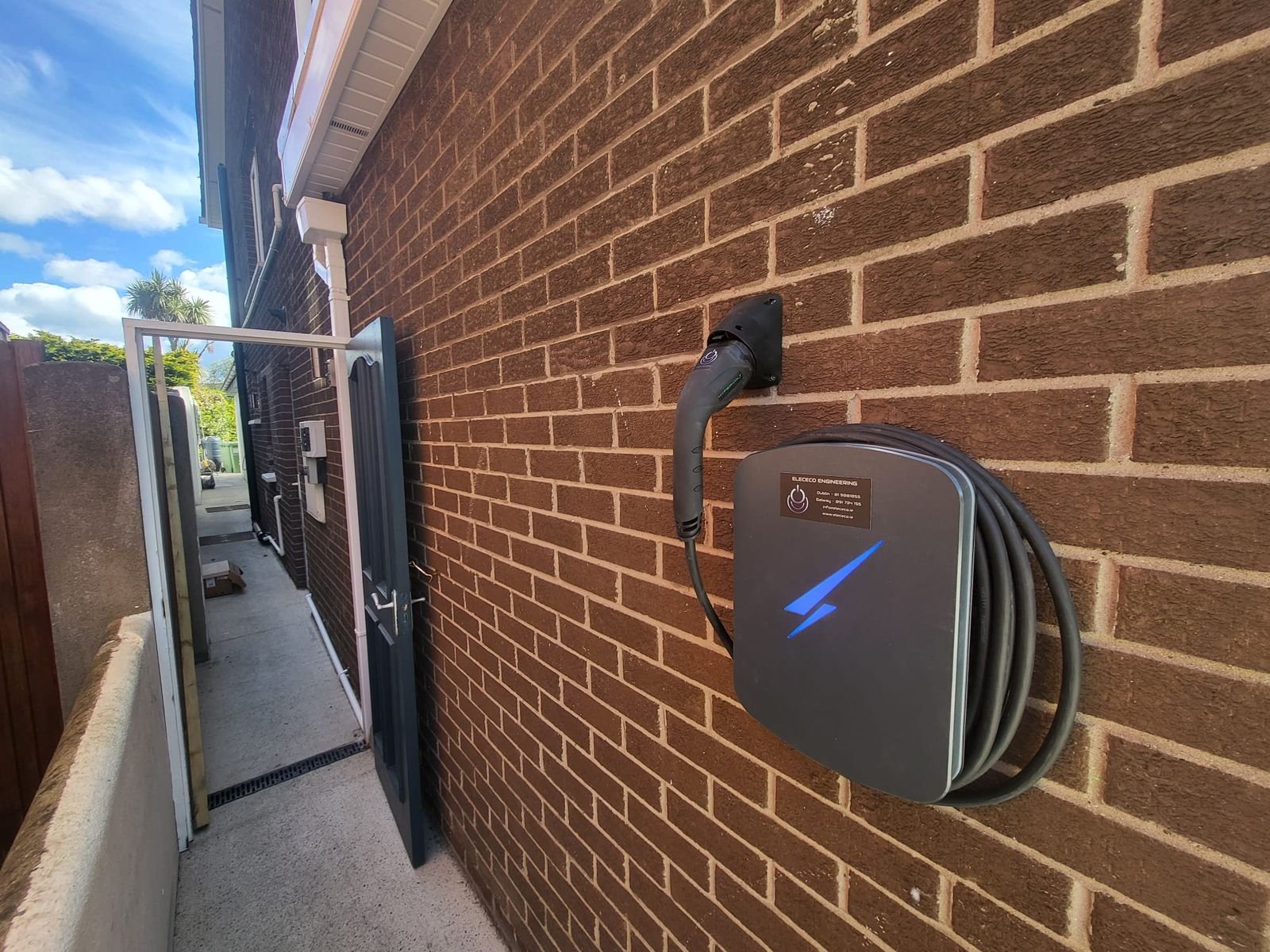 Black smart EV charger on a brick side passage wall, by Elececo Engineering