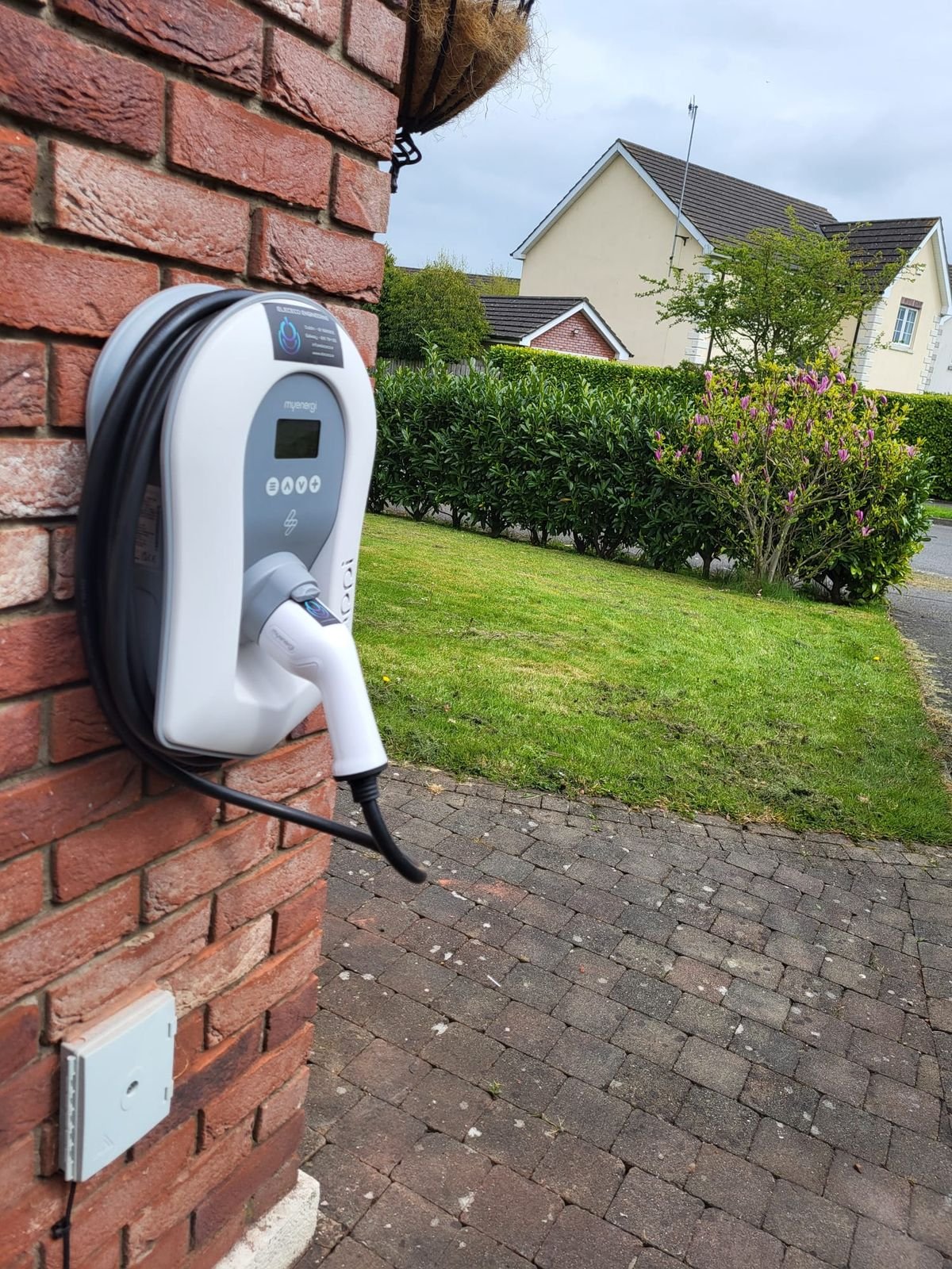 myenergi Zappi EV charger on a red brick wall beside a driveway